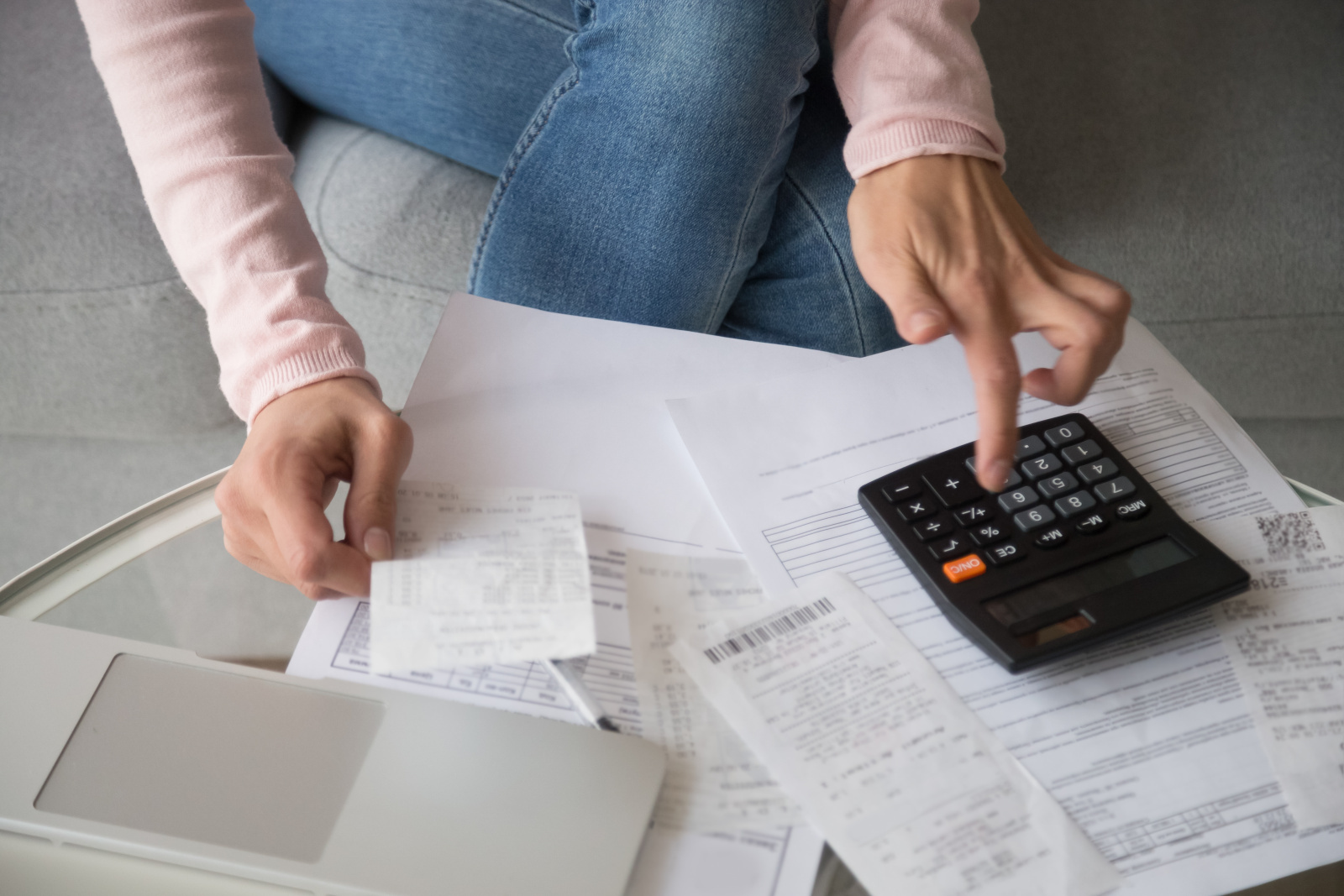 Ženska, ki v roki drži račun in računa na kalkulator. 